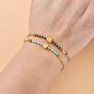 Delicate double layer bracelet featuring blue black beads and cute gold spiral shell charms.