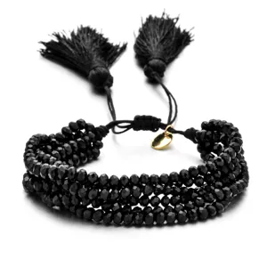 Primer plano detallado de pulsera trenzada de cuentas negras multicapa con borlas y dijes.