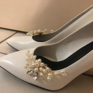 Detail view of handmade pearl rhinestone shoe clips on elegant white bridal high heels.