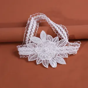 White lace wedding garter detail, elegant organza flower and pearl charm close up view.