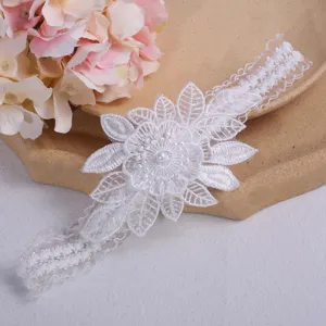 Detailed close-up of white lace wedding garter featuring floral applique and center pearl.