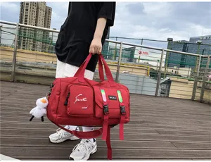 Outdoor detail shot of a red travel duffel gym bag with multiple pockets and cute duck pendant.