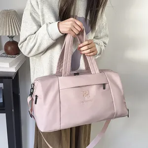Vue détaillée du sac de voyage rose clair avec poignées et bandoulière pour sport et loisirs.