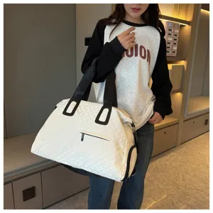 Detail shot of a large capacity quilted travel duffel bag in white with black handles.