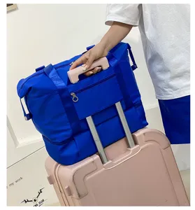 Blue travel duffel bag detail showing durable nylon material, pink handle and luggage sleeve.