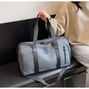 Détails du grand sac de voyage gris montrant un tissu résistant et des poches à fermeture éclair.