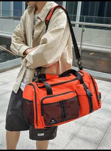 Outdoor detail view of a large orange travel duffel bag with mesh pockets and black shoulder strap.