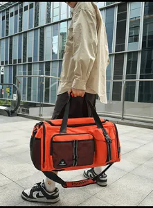 Outdoor detail view of the large capacity orange duffel bag, showing front pocket and strap.