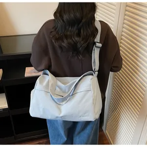 Vue détaillée du grand sac bandoulière en toile bleu clair avec large sangle et poches.