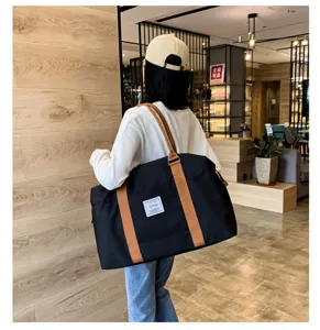 Vue detaillee du grand sac de voyage souple avec poignees marron, porte par le modele.