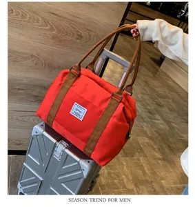 Sac de voyage rouge avec anses marron, vue de détail style de vie montrant grande capacité.