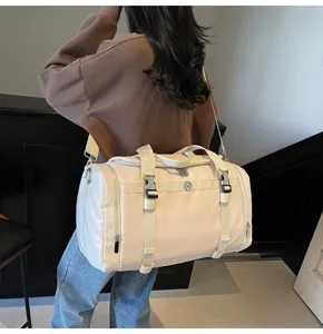 Back view detail shot of a lightweight beige travel duffel bag worn by a model indoors.