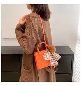 Detail view of stylish orange quilted mini handbag with chic scarf and plush ball charm.