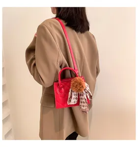 Detail view of a stylish red quilted handbag with cute pom-pom and scarf charm, worn by model.