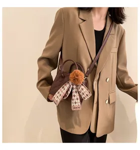 Detailed view of a trendy stylish crossbody shoulder bag featuring a cute pompom and patterned scarf.