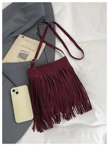 Detailed view of a chic burgundy suede fringe crossbody bag, stylish autumn and winter accessory.