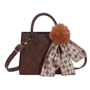 Brown quilted leather handbag featuring a fluffy pom-pom and elegant plaid scarf charm for women.