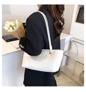 Detail shot of a stylish white glossy patent leather shoulder bag worn by a model in a clean room.