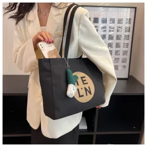 Detailed view of the black canvas tote bag with letter patch and cute pendant, stylish look.