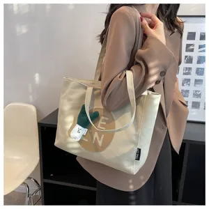 Detailed view of Korean style canvas tote bag with letter patch and green plush pendant.