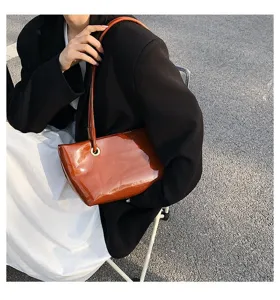 Glossy brown patent leather shoulder bag detail shot, elegant underarm tote for women.
