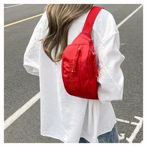 Detailed shot of the red crossbody chest bag showcasing vertical embroidered letters and zippers.