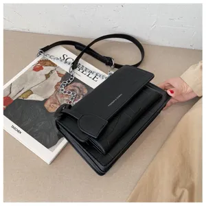 Black textured leather crossbody bag detail with metallic chain strap and flap design.
