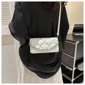 Detailed view of white quilted crossbody bag with metal chain accent in modern interior setting.