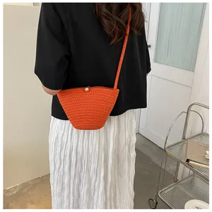 Detail view of a stylish orange woven crochet bucket bag with pearl detail worn outdoors.