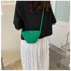 Detail view of the green woven crossbody bucket bag featuring a cute pearl closure button.