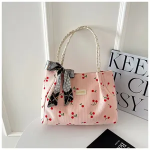 Détail de sac cabas en velours côtelé rose avec motif cerise, poignée tressée et foulard en soie.