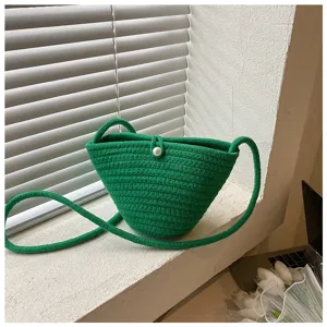 Detail view of a stylish green woven crossbody bag with pearl button closure and slim strap.
