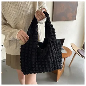 Detailed close-up view of the black pleated shoulder bag held by a model in a natural setting.