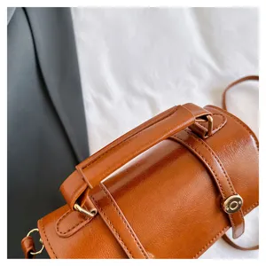 Détail de sac à main cylindrique marron, cuir PU brillant et quincaillerie métallique.