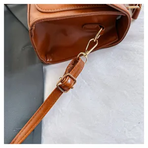 Détail de la bandoulière du sac en cuir marron, quincaillerie dorée, gros plan élégant du sac.