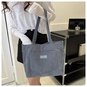 Grey corduroy tote bag detail shot, featuring front pocket and double shoulder straps.
