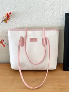 White tote bag detail showing pink straps, embossed texture, and front brand patch.