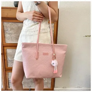 Detailed view of the pink embossed tote bag with a cute plush pendant, showing fine texture.