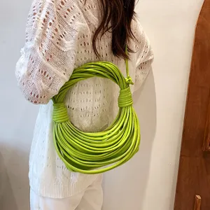 Detail view of a stylish bright green knotted noodle shoulder bag worn on a white knit top.