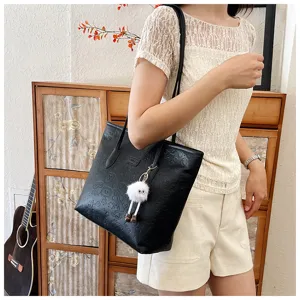 Black embossed large tote bag detail view, casual commuting shoulder bag with cute doll pendant.