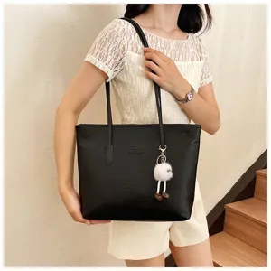 Close-up detail of the black embossed tote bag featuring dual handles and cute plush keychain.