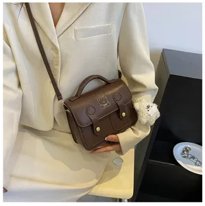 Detail view of retro PU leather mini satchel bag with cute bear emblem and plush pendant.