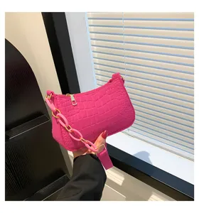 Dettaglio borsa a baguette in feltro rosa con stampa coccodrillo e catena spessa.