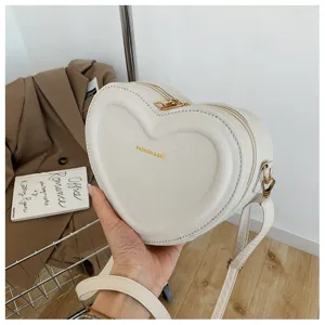White heart-shaped PU leather crossbody bag with chic golden hardware and zipper closure.