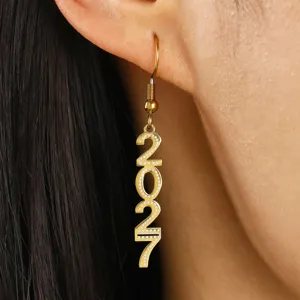 Close-up van gouden hangende oorbel met met strass steentjes ingelegde cijfers 2027