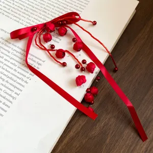 Close-up detail of a red fabric bow hair rope with beaded flower tassels on a book background.