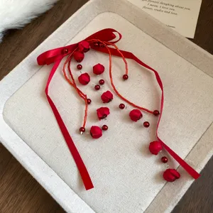 Red fabric rose bow hair rope closeup, elegant beaded tassel hair accessory detail view.