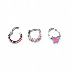 Detailed view of three stainless steel body piercing rings including red rhinestone and butterfly.