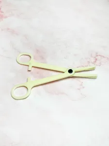 Acrylic body piercing tool detail shot showing the pale yellow clamping structure and handle rings.
