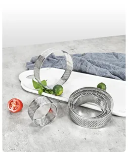 Detail shot of perforated stainless steel tart rings and mousse molds on kitchen prep surface.